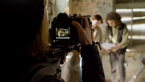 rear view of cameraman recording his coworkers reading a script in a ruined building