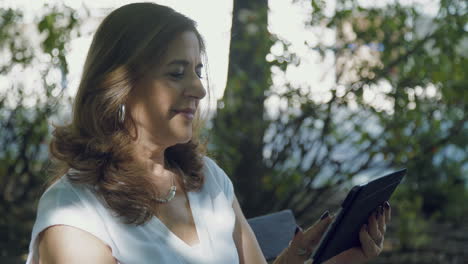 side view of elegant woman sitting outside, googling on tablet