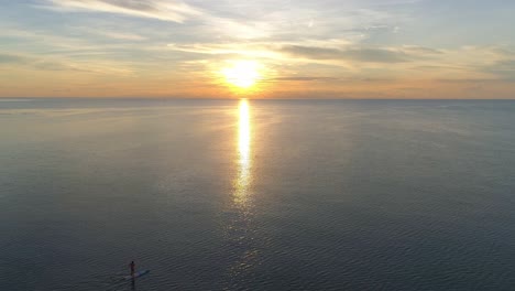 una silueta solitaria de paddleboarder contra la impresionante puesta de sol de la hora dorada sobre el océano