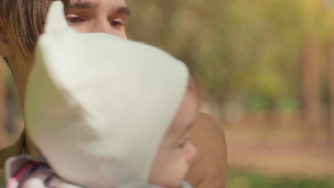 Ung hvid far holder baby i park, nært interaktion, far guider spædbarn til at røre blade, blid omfavnelse og sollys, ægte familiemoment der udtrykker kærlighed og forældreskab.