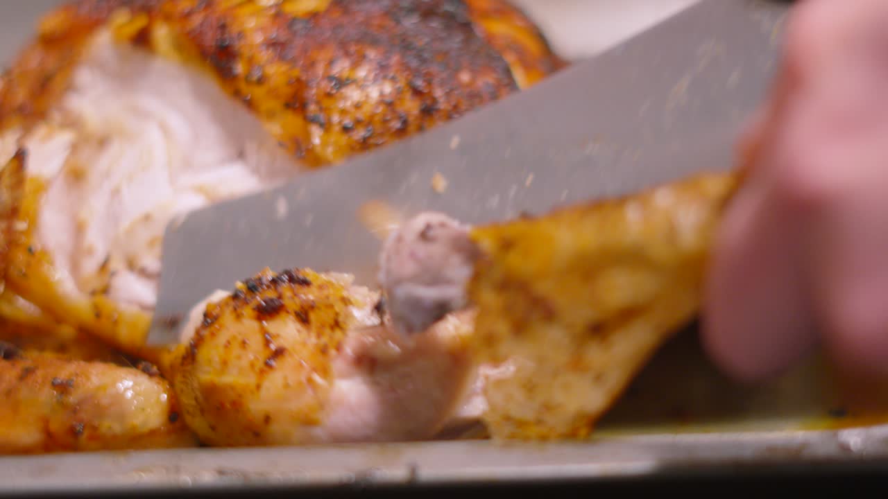 Chef Using Sharp Carving Knife to Remove Leg from Whole Roasted Chicken with Seasoned Crispy Skin