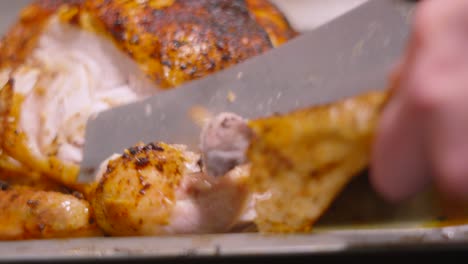 chef using sharp carving knife to remove leg from whole roasted chicken with seasoned crispy skin