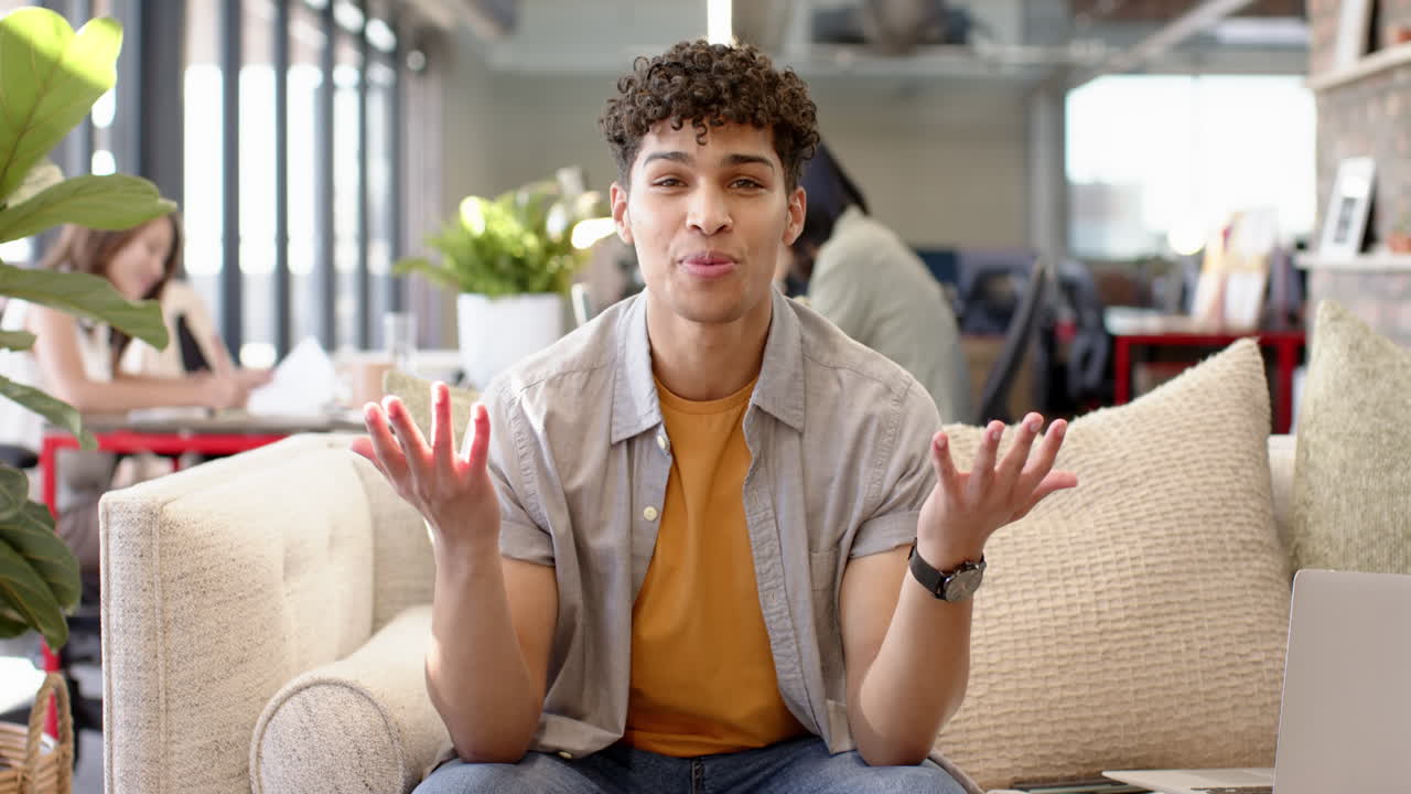 On video call, Talking and gesturing, young man sitting on couch in modern office space