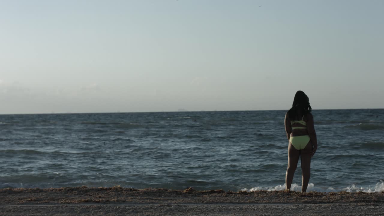 해변에 노란색 비키니와 손 제스처를 만드는 고독한 여자