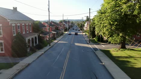 aerial drone flight above traffic, cars, trucks pass by traditional old homes along street, sidewalk, summer magic hour in united states of america, usa