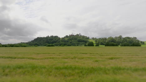 Drone-flies-over-field-of-wheat,-church-in-the-background