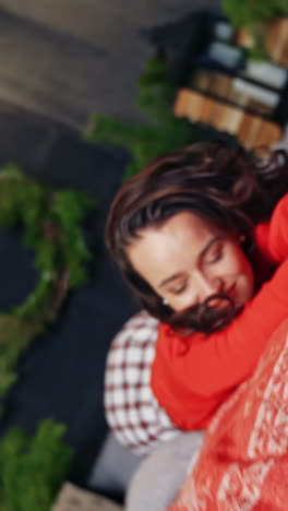 happy woman on christmas decorations background. young woman in red sweater is lying on the bed with pleasure in winter holidays. happy winter holidays concept. vertical video