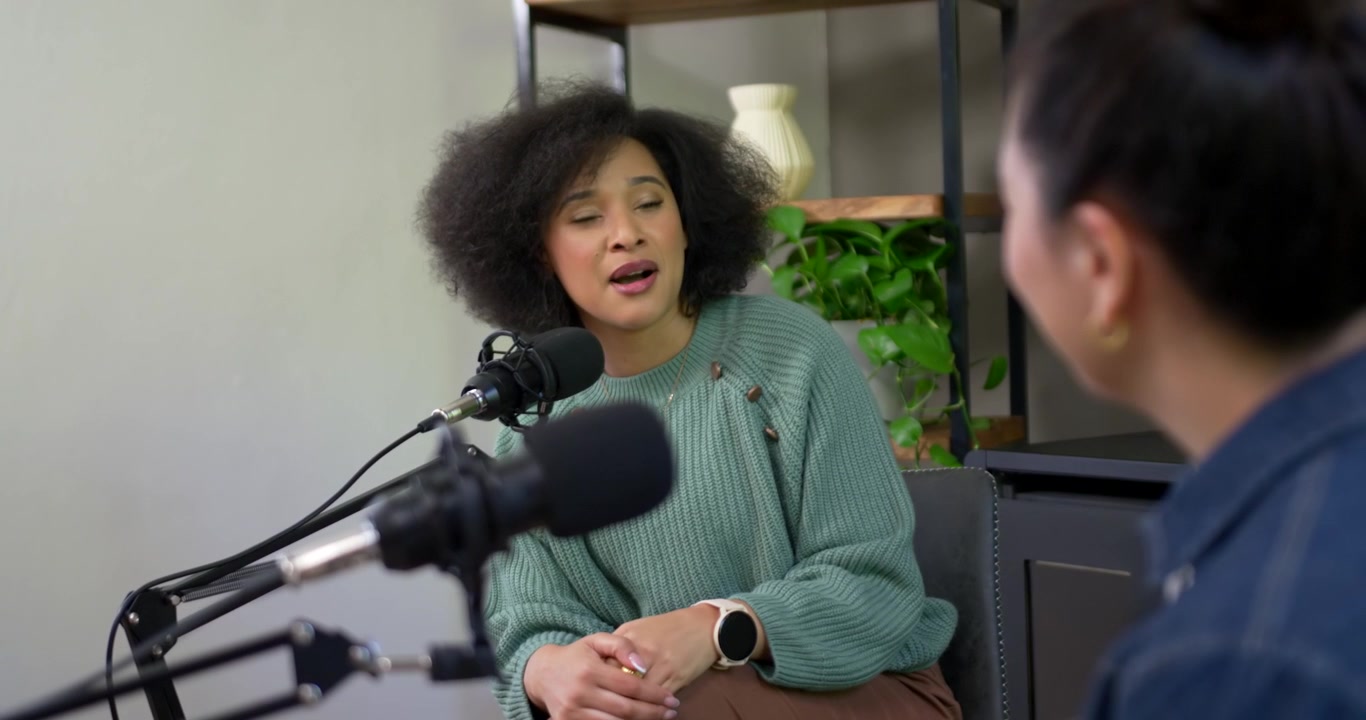 Mic going live, Diverse female hosts, green-sweater host speaking, gesturing during interview