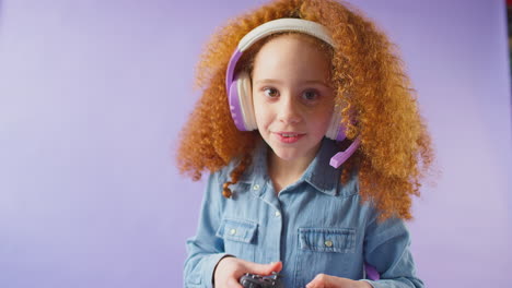 studio shot of girl wearing headset gaming with controller against purple background