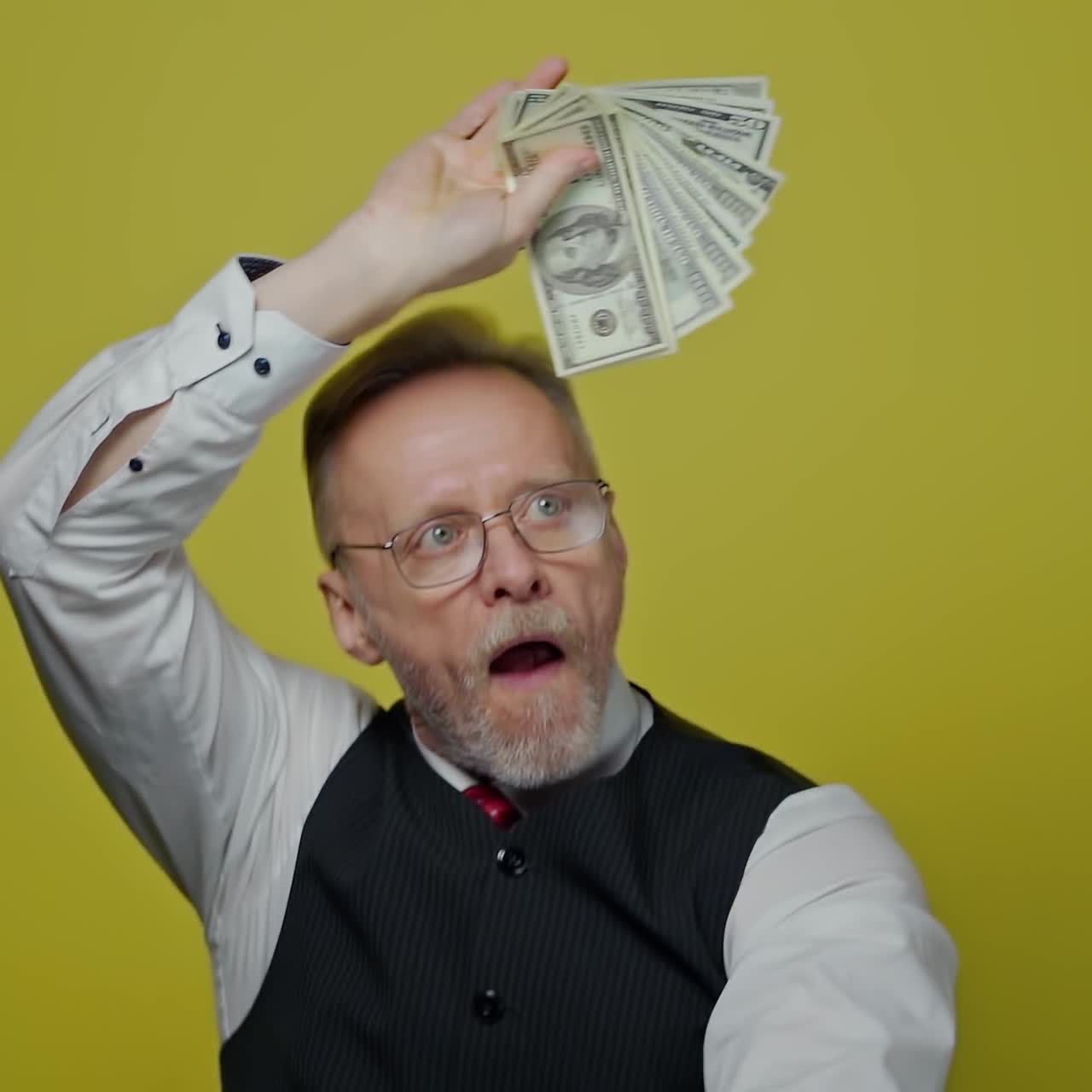Anziano divertente che sventola banconote da un dollaro. Molti soldi nelle mani dell'anziano. Uomo d'affari felice tiene dollari su sfondo giallo. Movimento lento