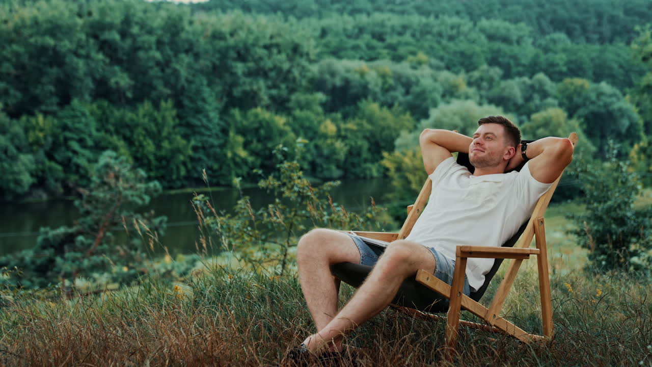 Happy man in a white t-shirt takes a break from work on his laptop. Man puts hands behind his head and relaxes in a chair.