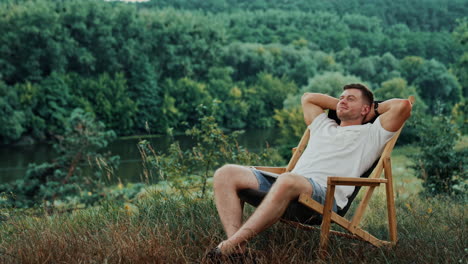 happy man in a white t-shirt takes a break from work on his laptop. man puts hands behind his head and relaxes in a chair.