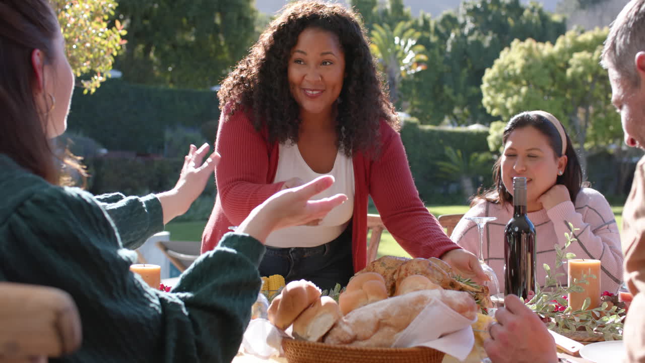 Des amis heureux et diversifiés servent un repas de célébration de Thanksgiving dans un jardin ensoleillé.