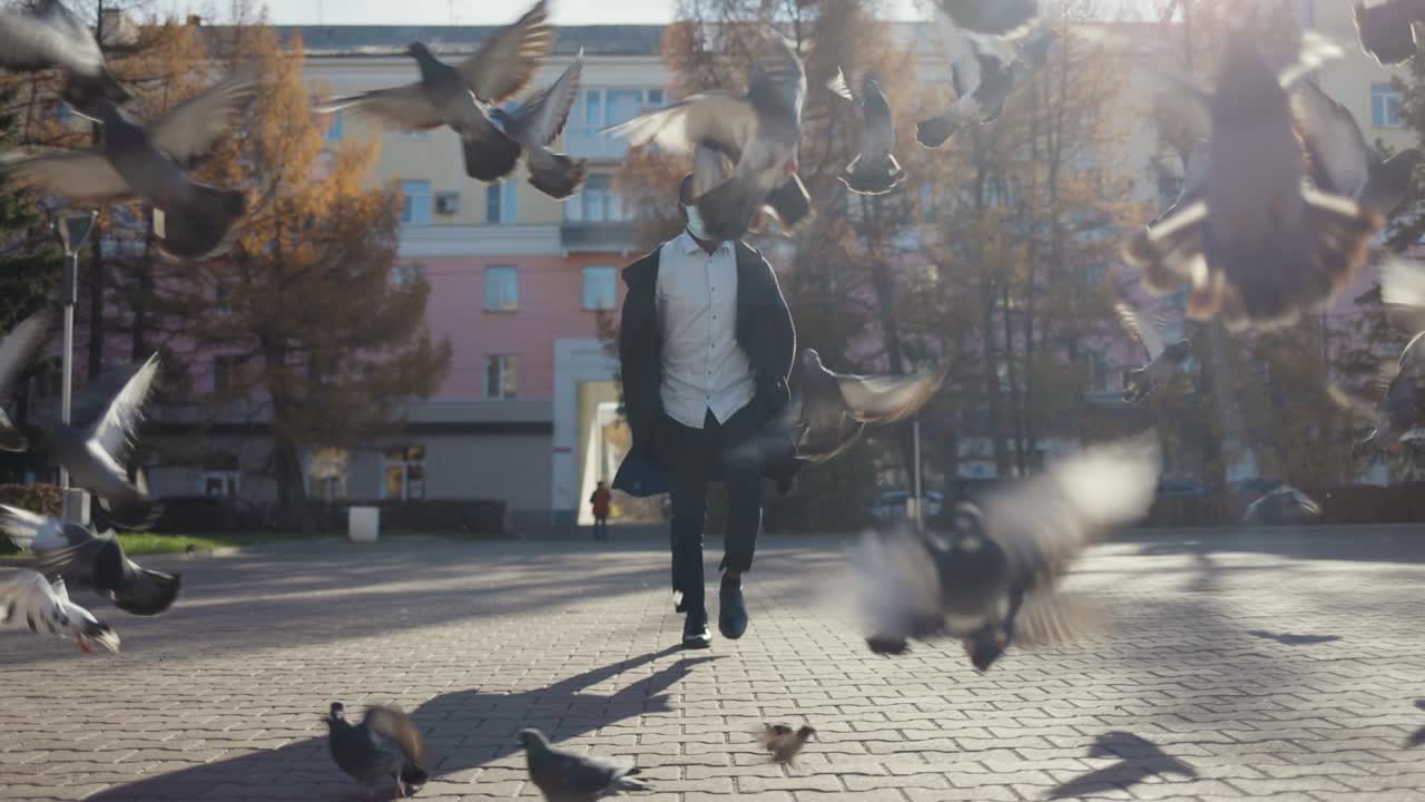 Man wearing a mask walking in a city square with pigeons
