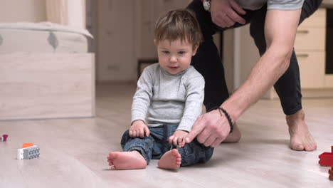 bebé sentado en el suelo de la sala de estar mientras su padre juega con los dedos de los pies