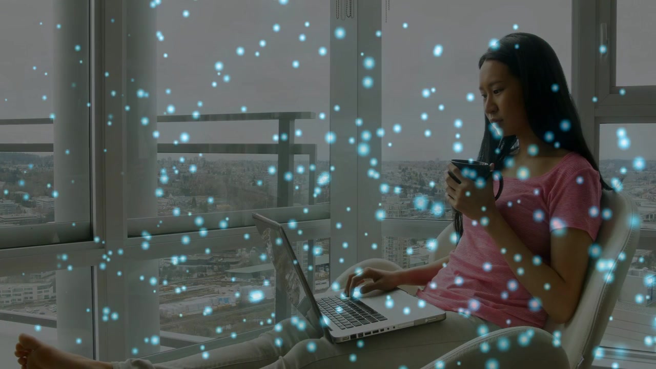 Woman typing laptop after phone ping, working by window with blue particles drifting in front