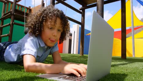 Vista-Frontal-De-Una-Colegiala-De-Raza-Mixta-Estudiando-En-Una-Computadora-Portátil-En-El-Patio-De-La-Escuela-4k