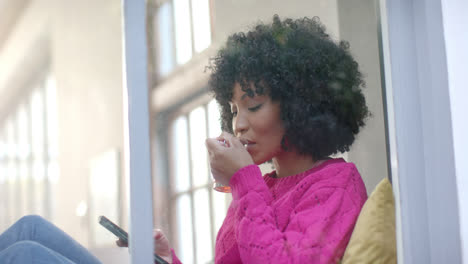 biracial woman drinking tea and using smartphone at home, slow motion