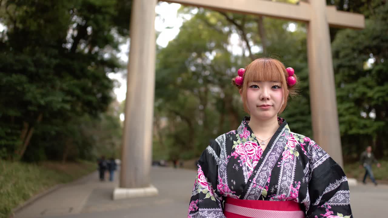 Una giovane donna che indossa un kimono floreale è in piedi fuori da un santuario sotto la luce naturale del giorno