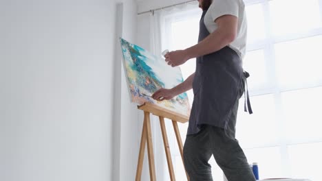 a young male artist works in a studio he uses bright paint on a large white canvas - a young male artist works in a studio, he uses bright paint on a large white canvas. a modern and successful masterpiece of drawing by an artist of abstract art