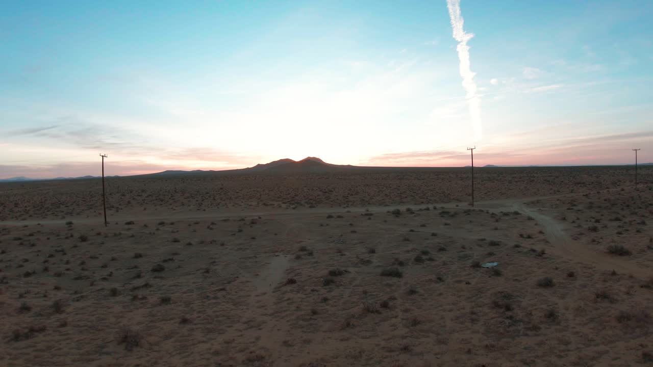 Flying low over the Mojave Desert landscape, under the power lines and over a dirt road towards two mountains at sunrise