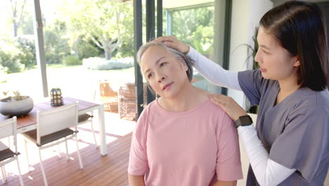 physiotherapist assisting senior asian woman with neck exercises at home therapy session