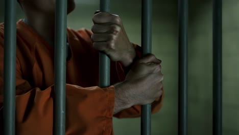 person in orange jumpsuit gripping prison bars