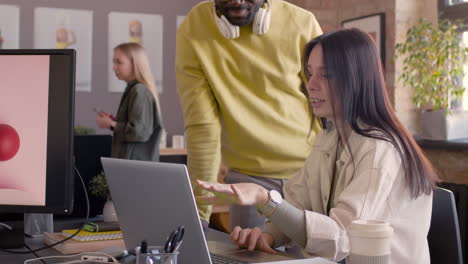 smiling female graphic designer explaining project on laptop computer to her colleague in an animation studio 1