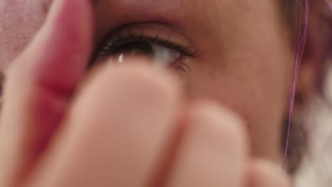 Extreme-close-up-of-young-woman-with-purple-hair-examining-her-bloodshot-eye