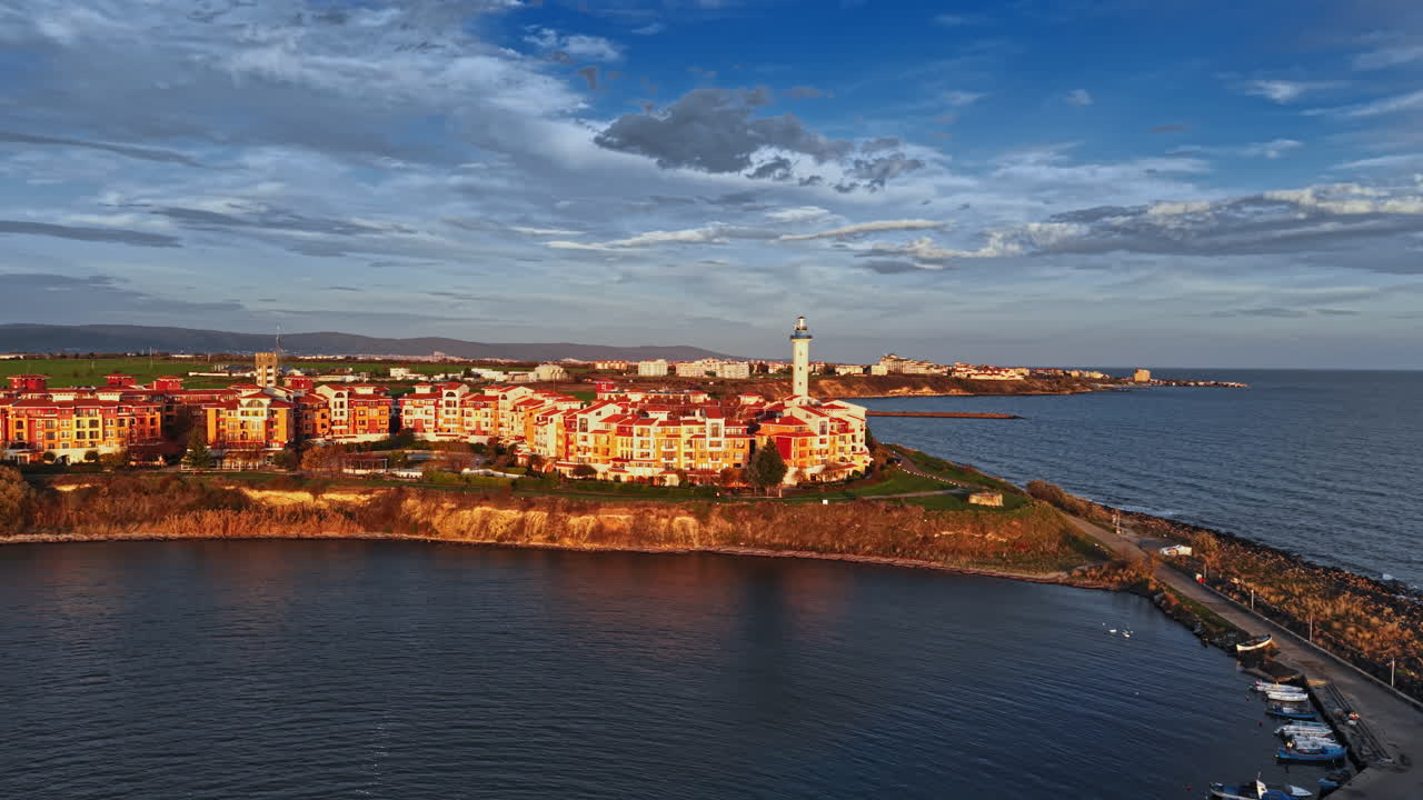 Vista panoramica della costa con un faro storico affacciato sul mare calmo e un'incantevole città durante un tramonto dorato