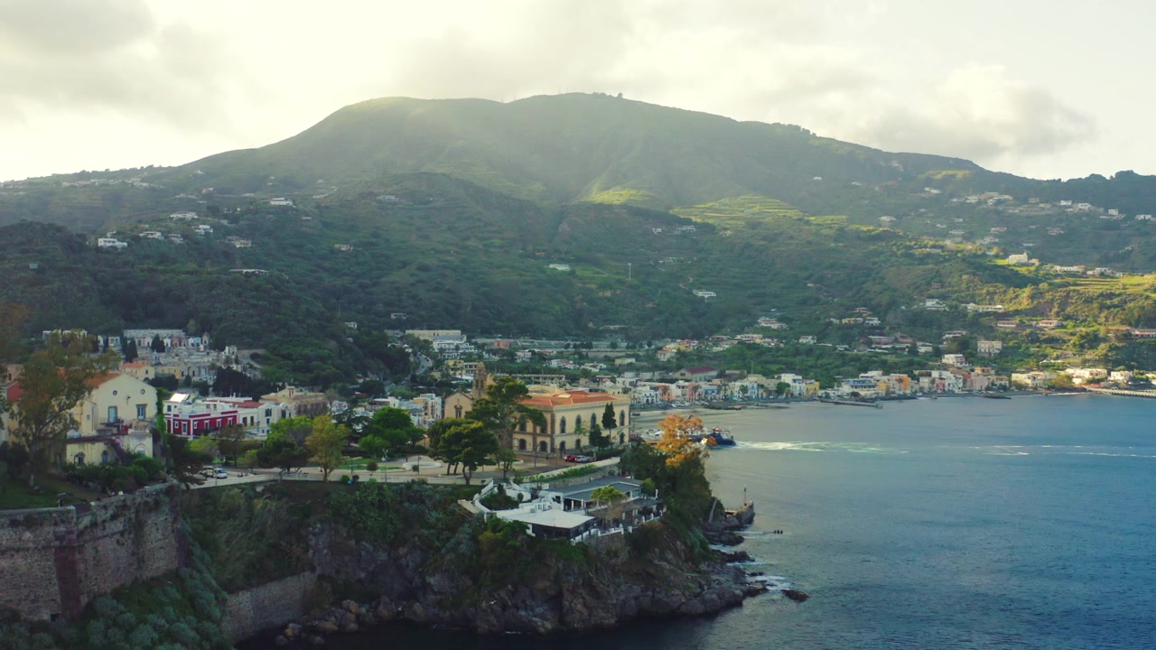 Cidade de Lipari revelada do alto de falésias costeiras durante a hora dourada - plano aéreo de estabelecimento, Ilhas Eólias, Itália