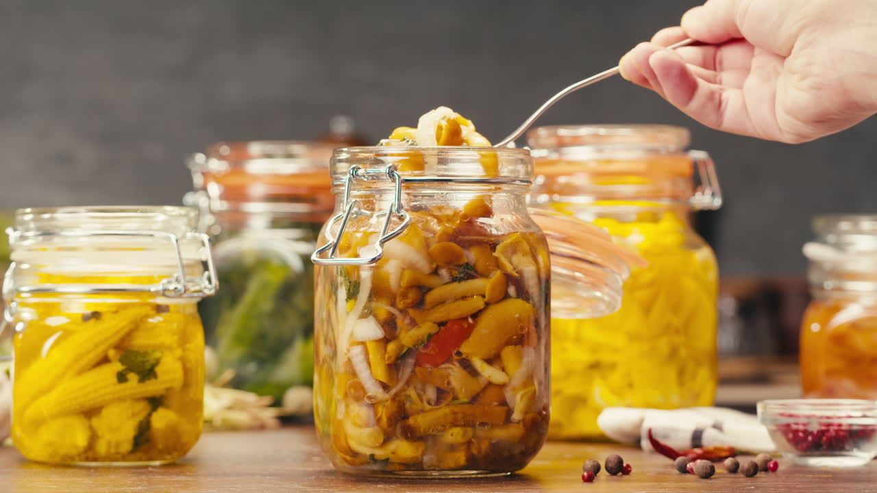 Fermented food in glass cans on table close-up. Preservation of vegetables in glass jars. Fermentation preserved mini corns, kimchi, cucumbers, mushrooms with spices.