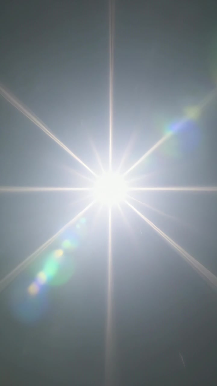 Video verticale: Sole radiante che crea un effetto starburst e riflessi dell'obiettivo nel cielo, con il bagliore che satura il sensore