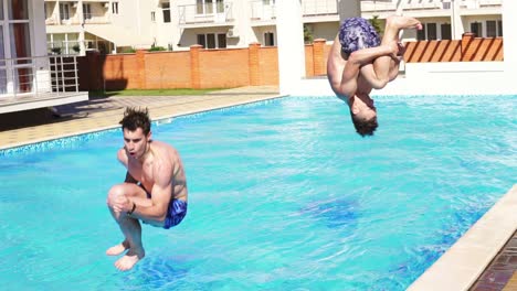 two young athletic men in swimshorts running and jumping to the swimming pool turning around. slowmotion shot.