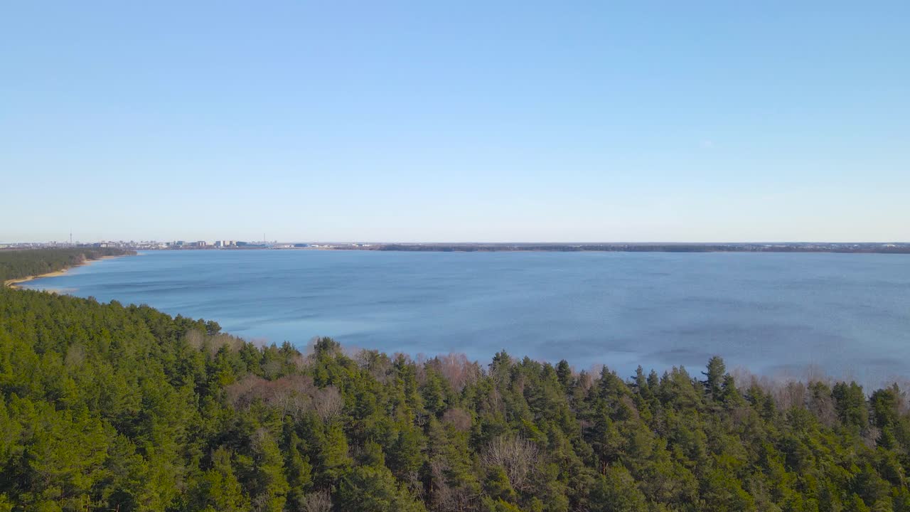 Aerial drone footage view of Ülemiste lake or järv during a gorgeous sunny day in Tallinn. The Estonian water resevoir is surrounded by a vibrant green pine forest and Tallinn city is in background.