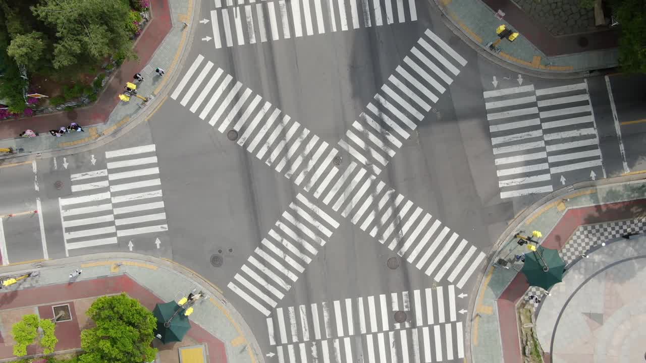 A dynamic and cinematic drone shot spiraling upwards while rotating over a four-way intersection in a South Korean school zone. The footage prominently features the distinctive yellow crosswalks and '