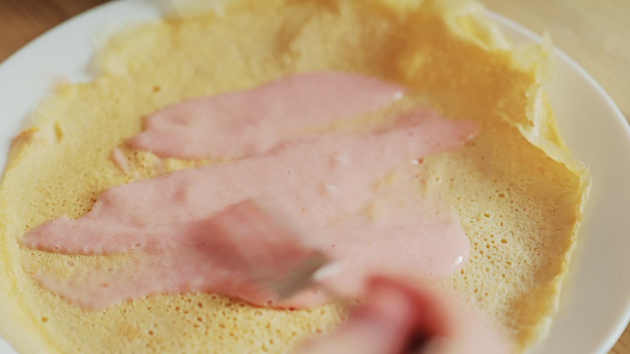 Fresh strawberry milk sauce being gently spread on soft crepe with silver fork