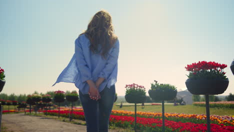 back view of relaxed girl with camera walking in summer flower park in sunshine.