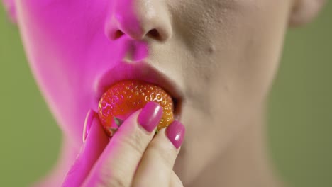 cerca de la boca de la mujer tomando un bocado y comiendo fruta de fresa, estudio filmado con iluminación colorida