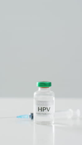 video vertical de la vacuna contra el hpv y la jeringa en una mesa blanca, con fondo gris y espacio para copiar