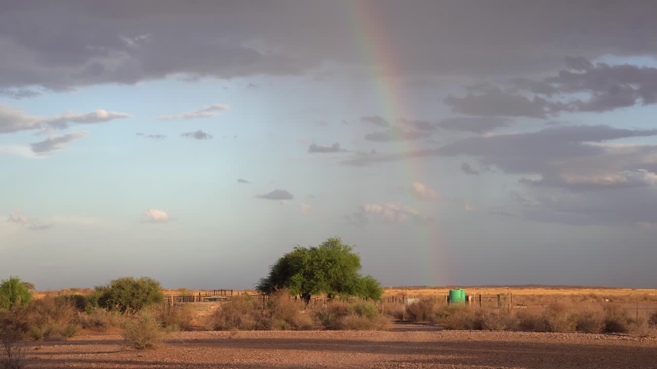 toma todavía estable de un arco iris en la distancia, con un recinto de ovejas al frente en una granja de ovejas en namibia