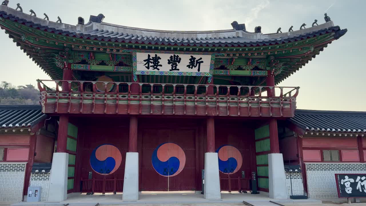 Vista frontale del padiglione del cancello principale presso la Fortezza di Suwon Hwaseong, caratterizzato da un tradizionale tetto coreano in tegole, struttura in legno dipinto, mura della fortezza e porte circolari del cancello
