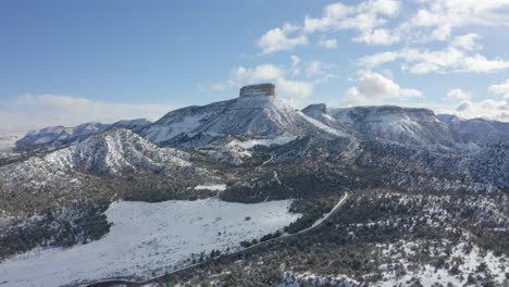 las imágenes de drones muestran una carretera que recorre una cadena montañosa cubierta de nieve con un pico afilado cubierto de vegetación escasa en un día soleado