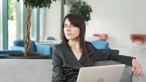 Retrato-De-Una-Mujer-Joven-Y-Hermosa-Con-Traje-Y-Computadora-Portátil,-Sentada-En-Un-Centro-De-Negocios,-Sonriendo-Y-Mirando-A-La-Cámara