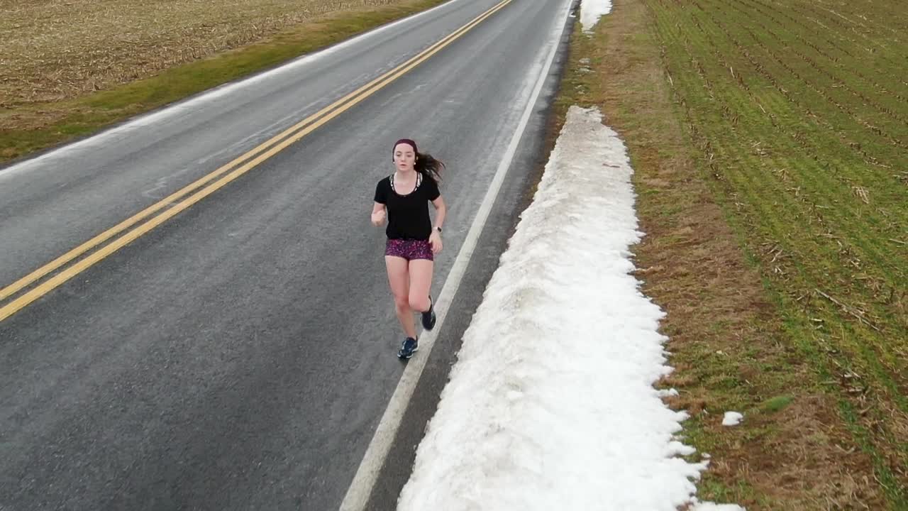 tiro de seguimiento de corredora, primer plano de una adolescente haciendo ejercicio, actividad cardiovascular, nieve a lo largo del costado de la carretera en pensilvania, ee.uu., cámara lenta