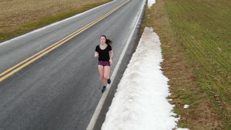 female runner tracking shot, close-up of teenage girl exercising, cardio activity, snow along side of road in pennsylvania usa, slo-mo