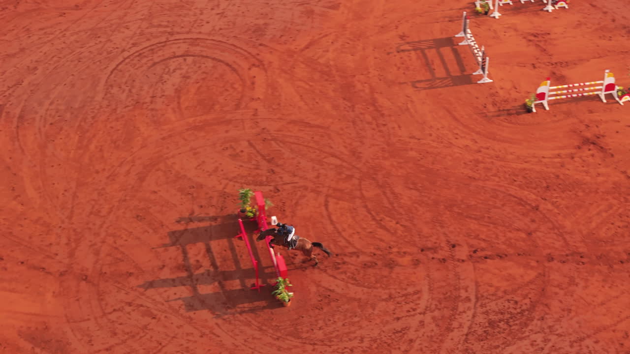 Aerial view of rider and horse during jumping exercise on red dirt equestrian arena