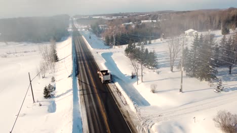 Aerial-drone-shot-tracking-a-truck-ploughing-snow-off-the-interstate-after-a-heavy-snow-storm,-Vaughan,-Ontario,-Canada
