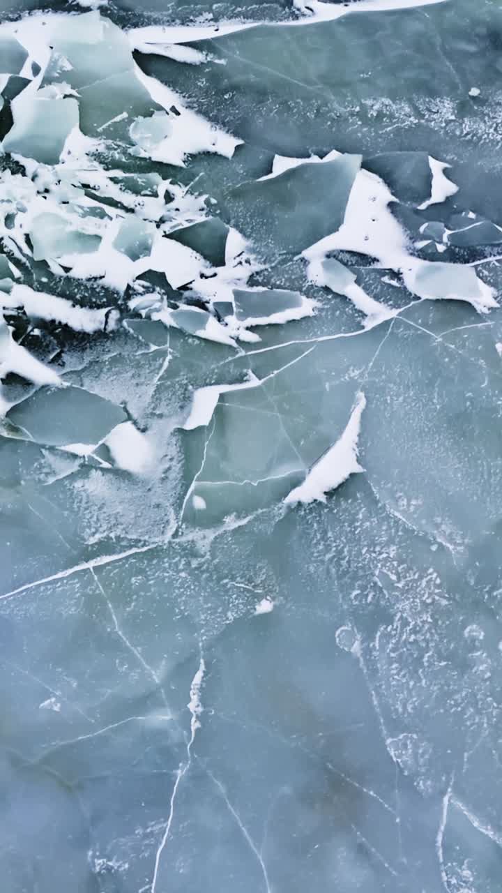 Lastra di ghiaccio blu-grigio incrinata con pezzi rotti frastagliati e polvere di neve, che mostra una superficie sottile e fragile e il concetto di pericolo invernale. Trama astratta minimale con spazio per il testo, verticale.