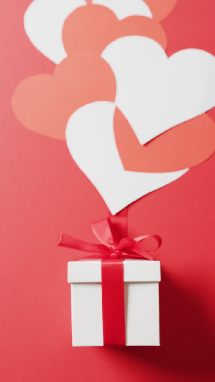 video vertical de caja de regalo blanca con arco rojo y corazones rojos y blancos, sobre fondo rojo